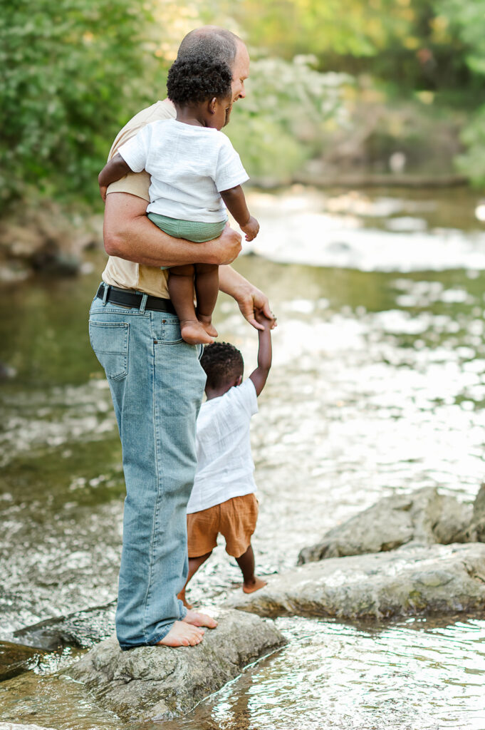 Dad holding children on rocks in creek during family session at Mill Creek Preserve in York PA