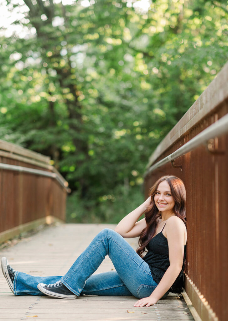 Senior girl sitting on wooden bridge at Mill Creek Preserve in York PA during golden hour session