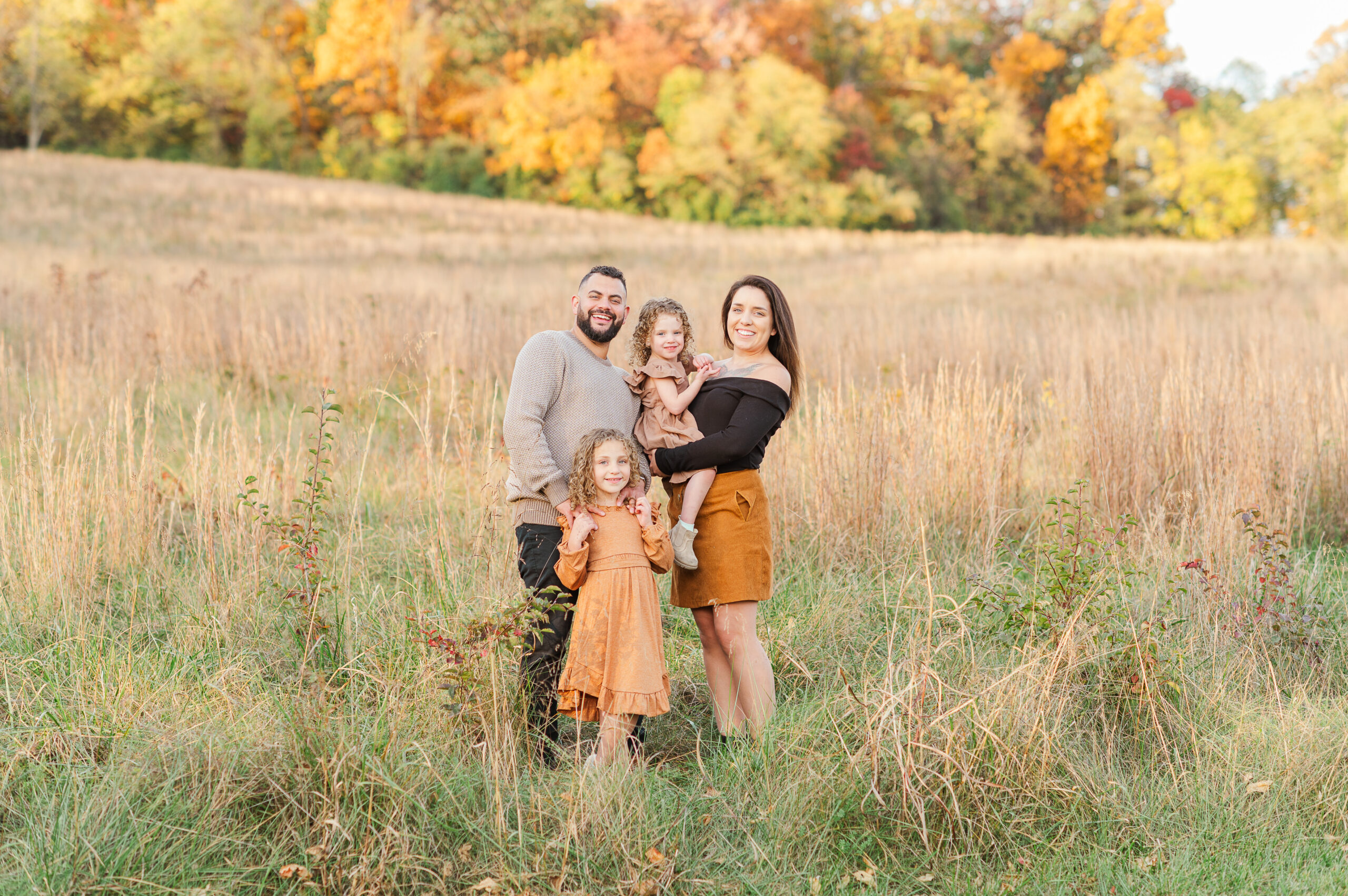 Family of four standing in tall grass during golden fall mini session at John Rudy Park