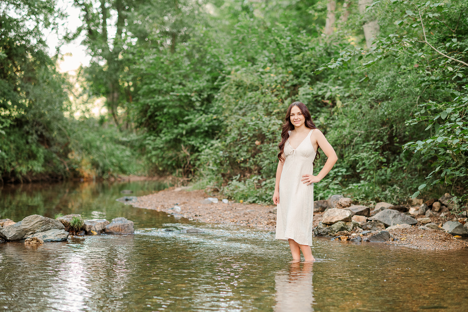 Senior girl standing in a creek wearing a pink dress at golden hour in Lancaster, PA