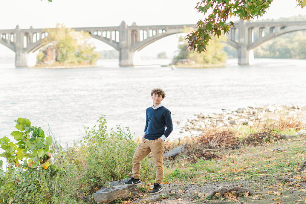 high school senior boy standing by Susquehanna River with Columbia Wrightsville Bridge at John Wright Restaurant in Wrightsville PA