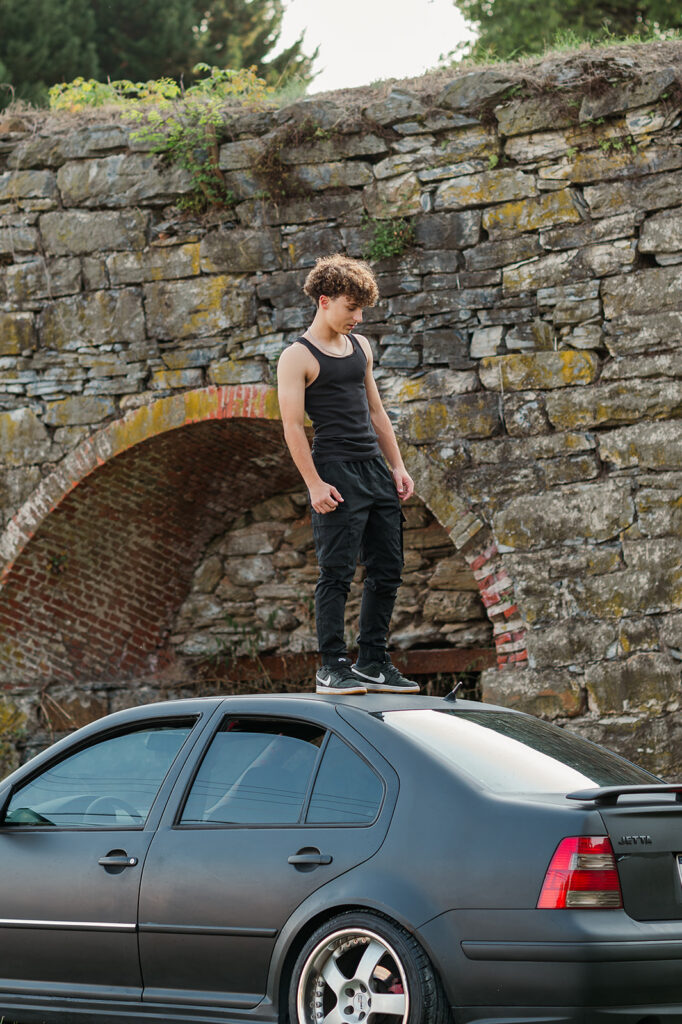 senior photos at John Wright Restaurant in Wrightsville PA with high school boy standing on car near stone wall