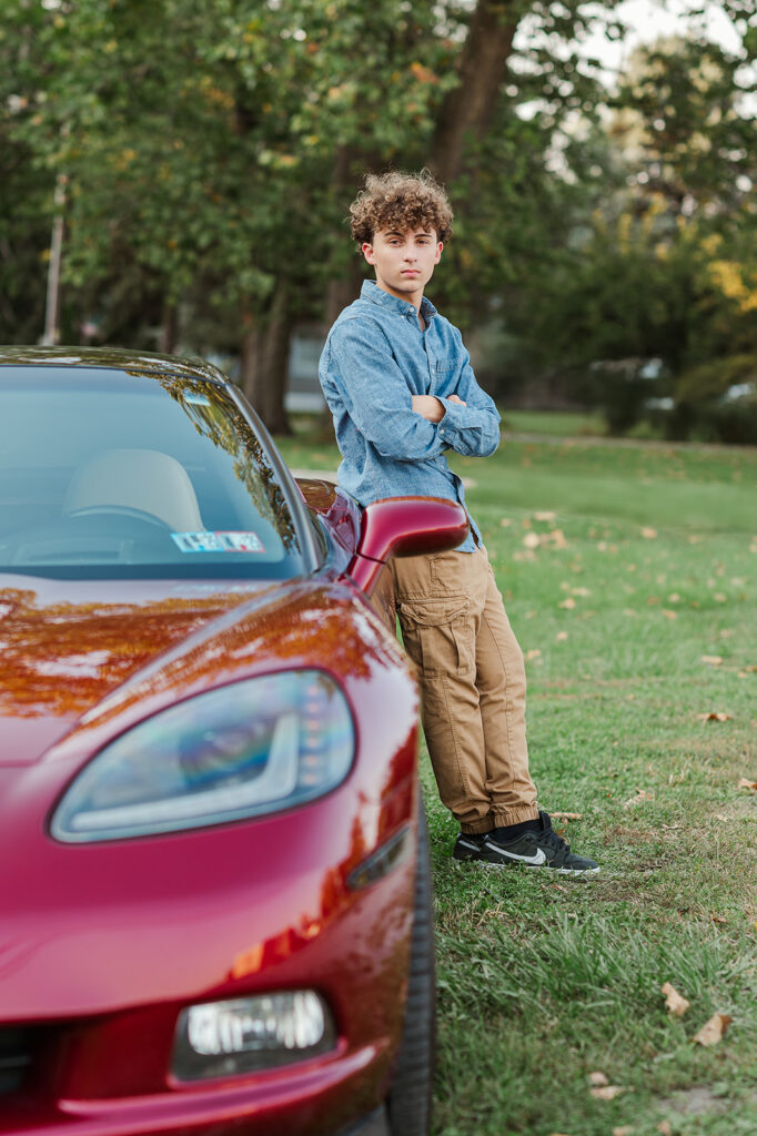 high school senior boy leaning on red car during senior portrait session at John Wright Restaurant in Wrightsville PA