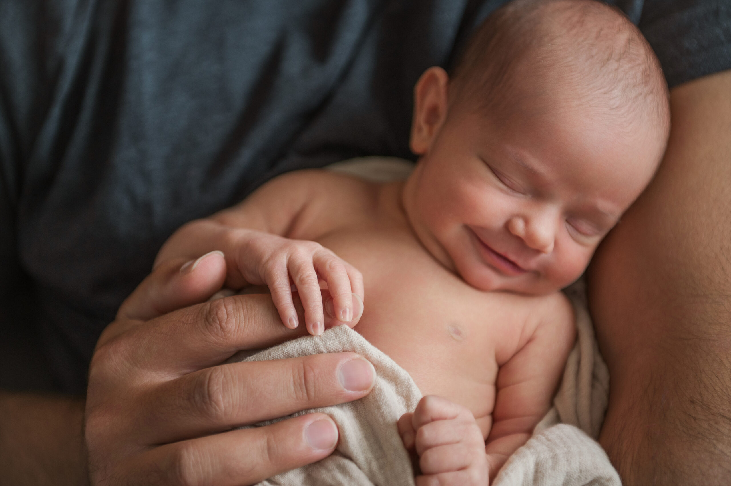At-home newborn photography in York PA with baby smiling in parent’s arms.