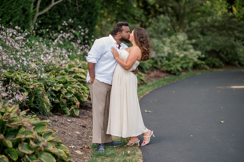engaged couple sharing a kiss during outdoor engagement session with greenery and flowers
