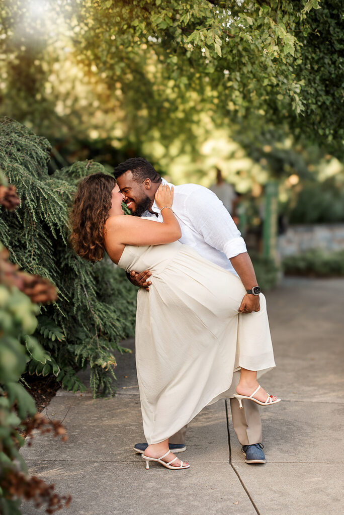 engaged couple sharing a dip kiss during engagement session with greenery background