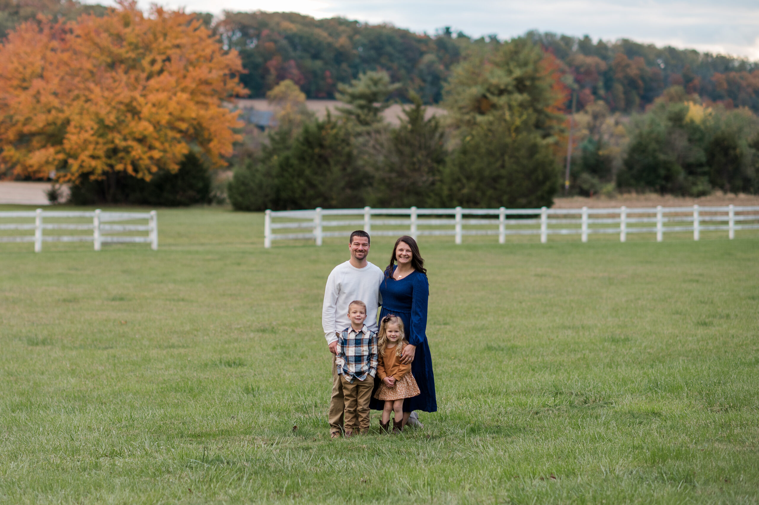 Family of four during a relaxed fall family photo session in York, PA with open field and white fence