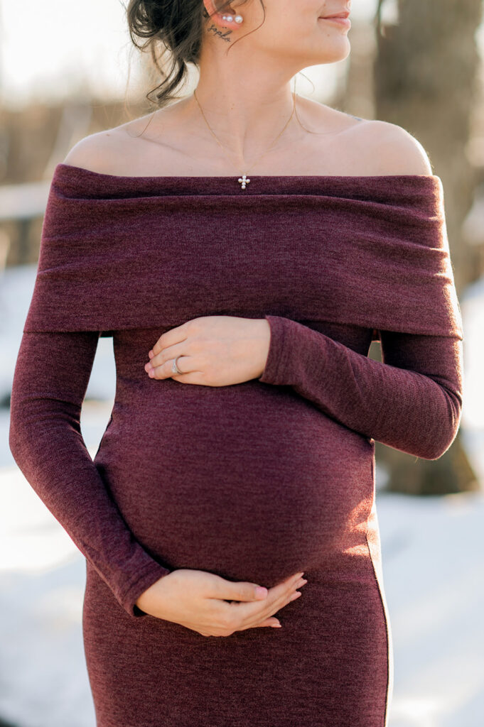Close-up of pregnant woman holding baby bump during outdoor maternity portrait session.