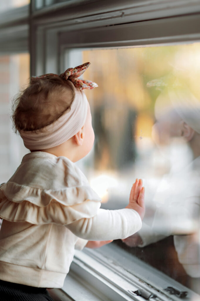 Baby girl looking out a window during an in-home sitter milestone photography session in Lancaster Pennsylvania