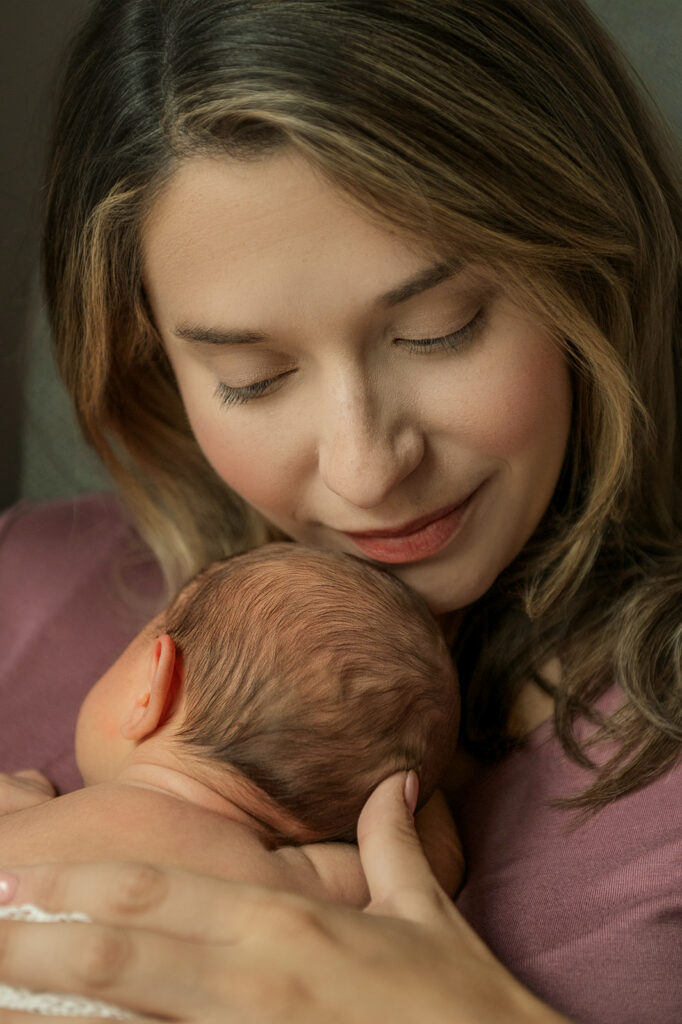 mom sitting on bed holding newborn baby in natural light