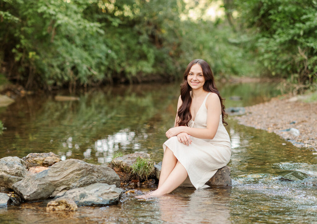 high school senior in a neutral dress sitting in a creek during outdoor senior portraits in York PA