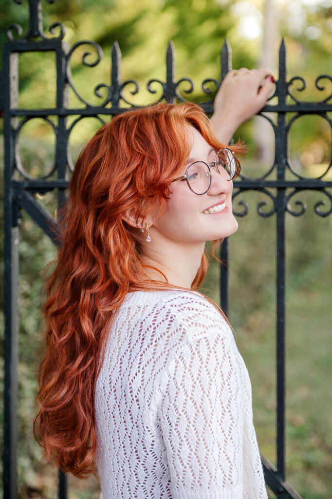 high school senior with red hair smiling near iron gate during Lancaster PA senior photo session