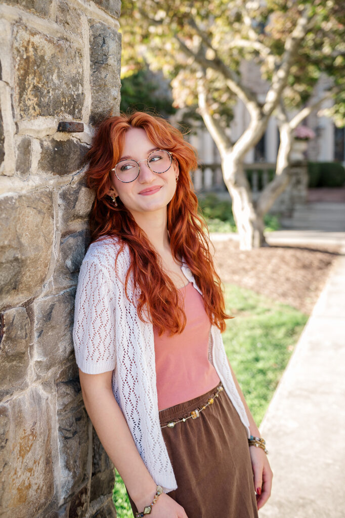 high school senior with red hair leaning against stone wall during senior photo session in York PA
