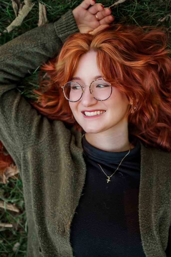 close up of high school senior with red hair laying on grass during senior photo session in Central PA