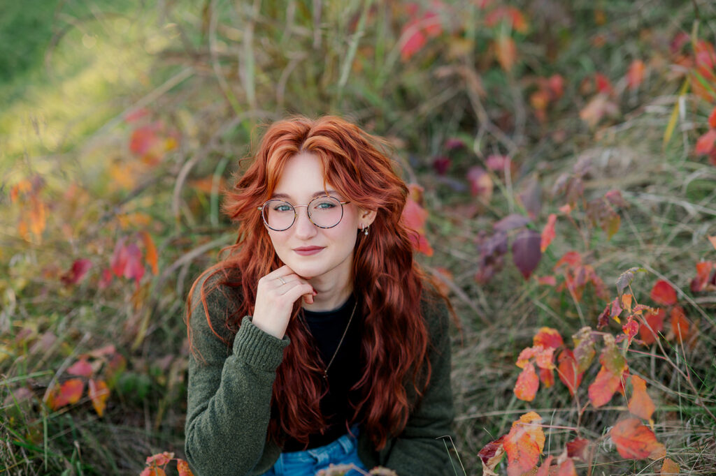 close up of high school senior with red hair surrounded by fall foliage during senior photo session in Central PA