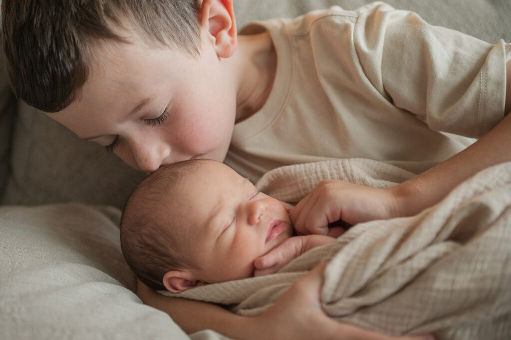 young sibling sitting and holding newborn baby