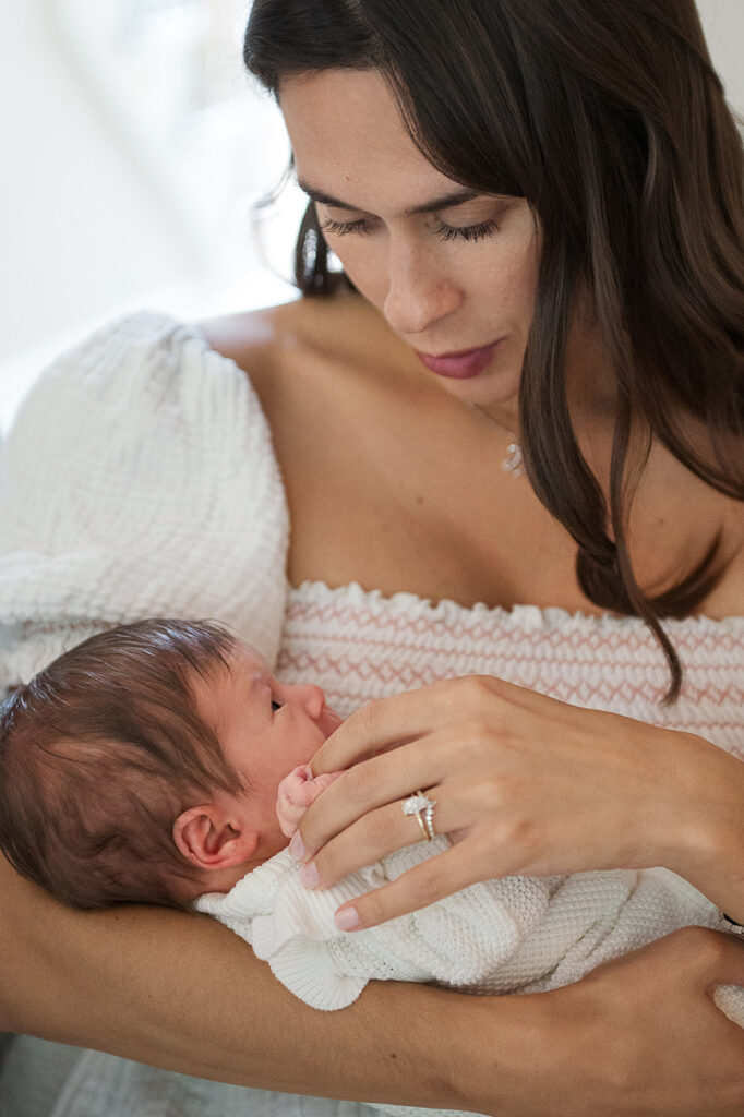 mom holding newborn baby in soft neutral outfit near window light