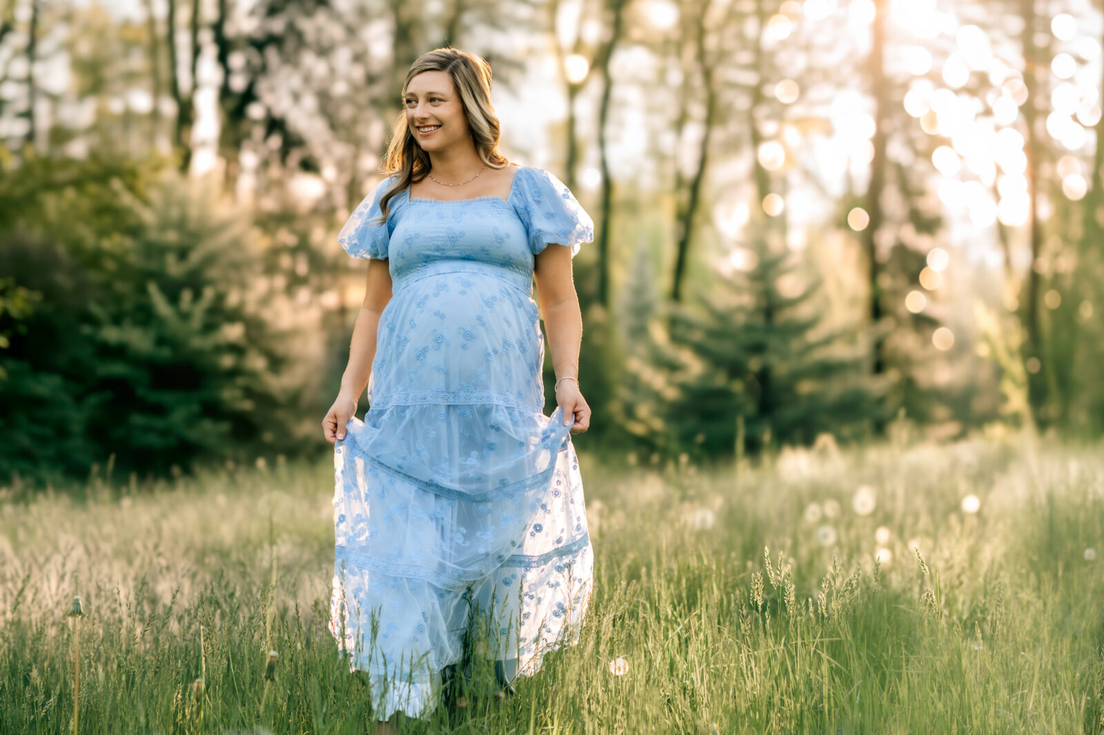 Maternity photos in York PA of a pregnant mom in a blue dress walking through a sunlit field at golden hour