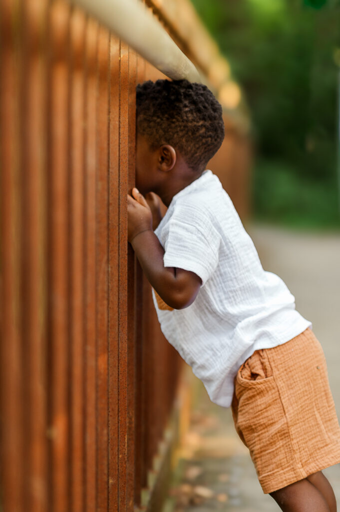 Young child peeking through a wooden bridge railing during an outdoor family photo session in York, PA