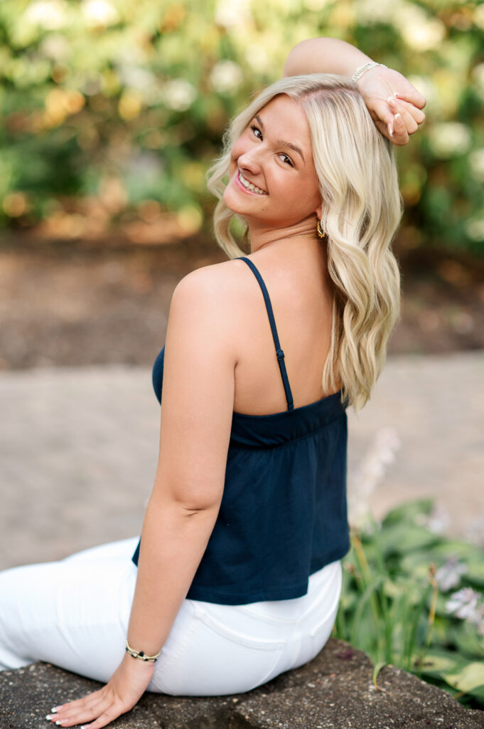 senior sitting near fountain with greenery in the background