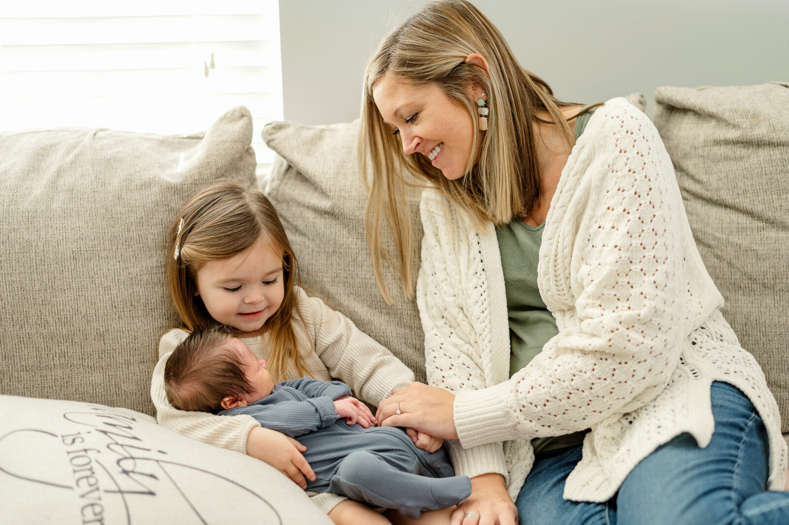 Lifestyle newborn photos in York PA of mom with her two children sitting on a couch holding their new baby