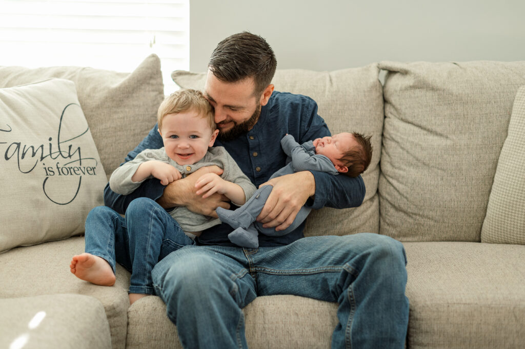 Dad holding a newborn and toddler on a couch during a lifestyle newborn photography session in York, PA