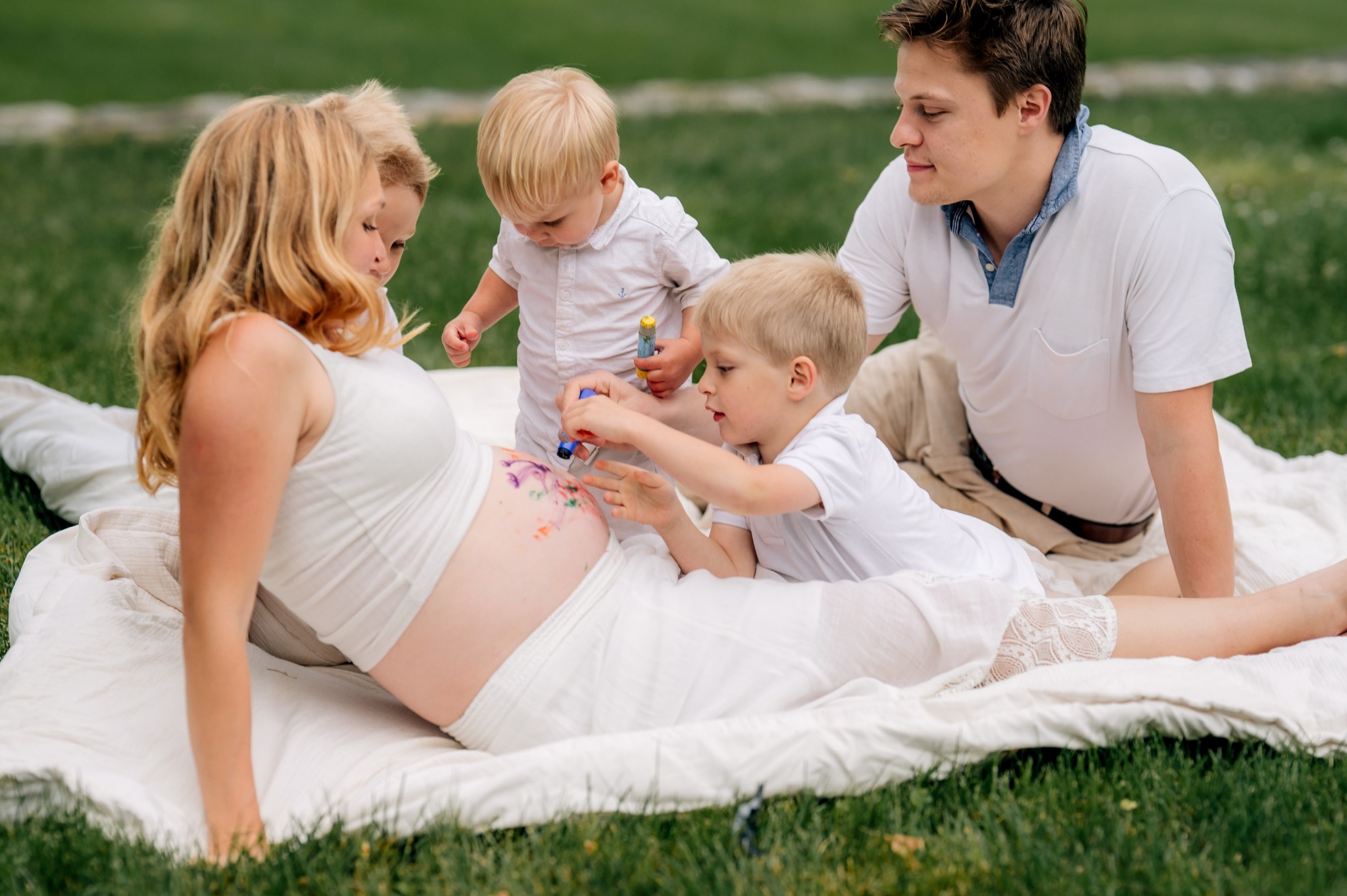 Family painting a rainbow on mom's baby bump to celebrate their baby