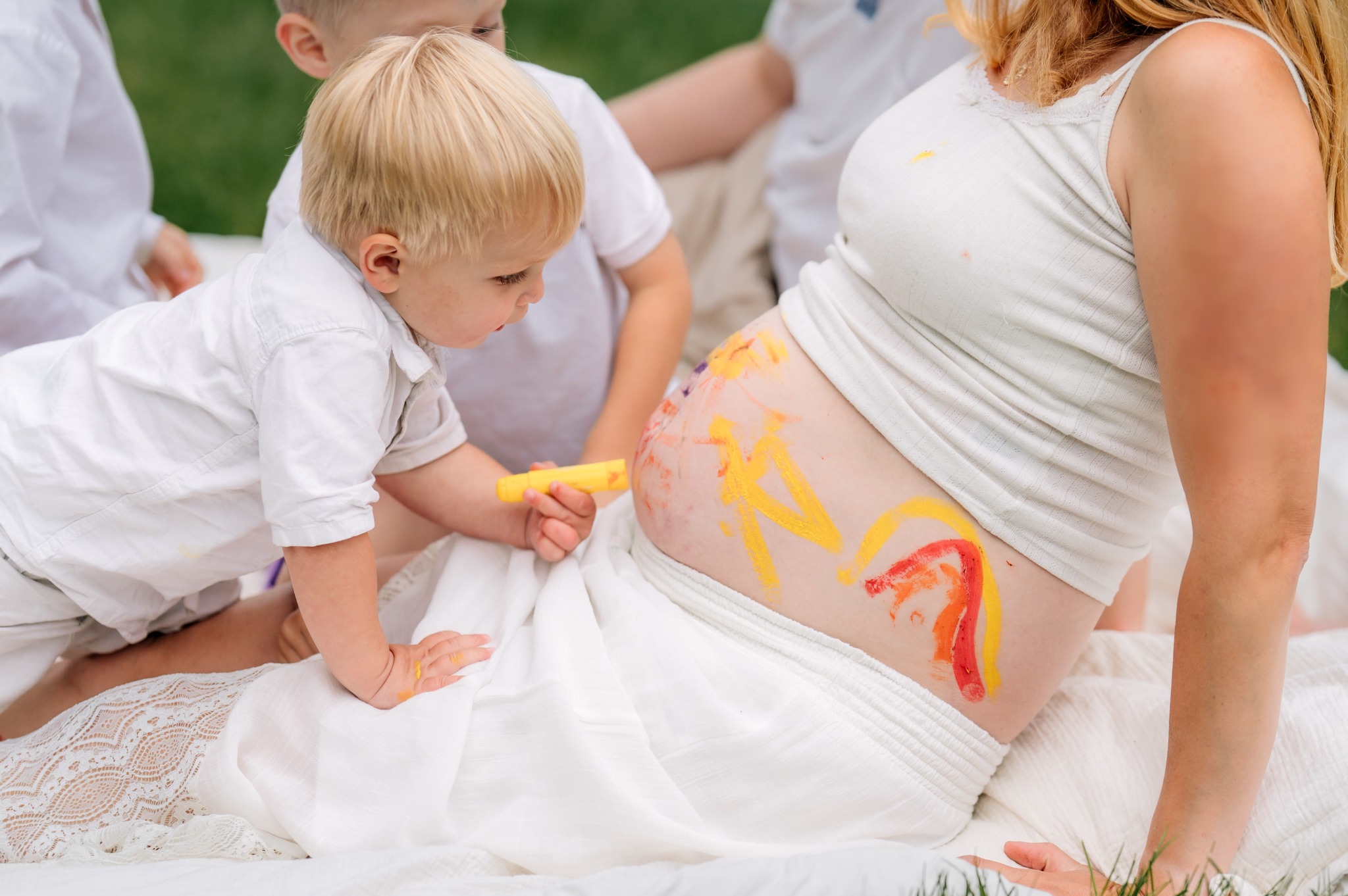 Young child painting a colorful rainbow on a pregnant mother's belly