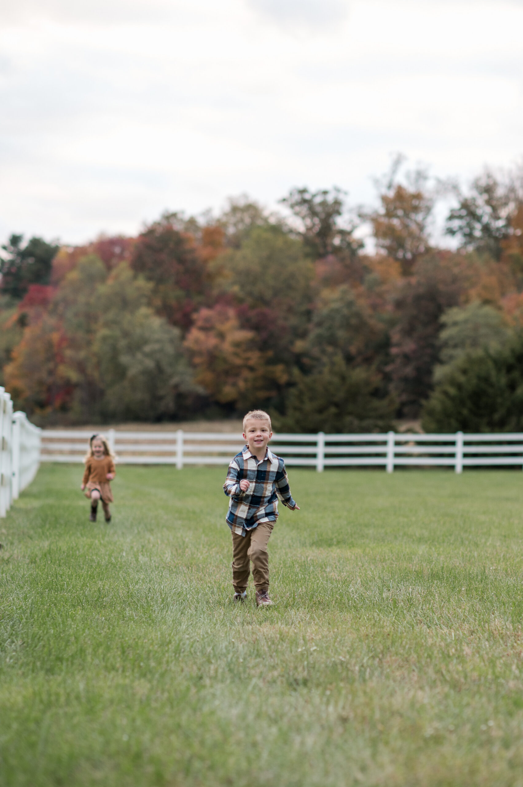 Two young children running through an open field surrounded by colorful fall trees during a family mini session in York, PA