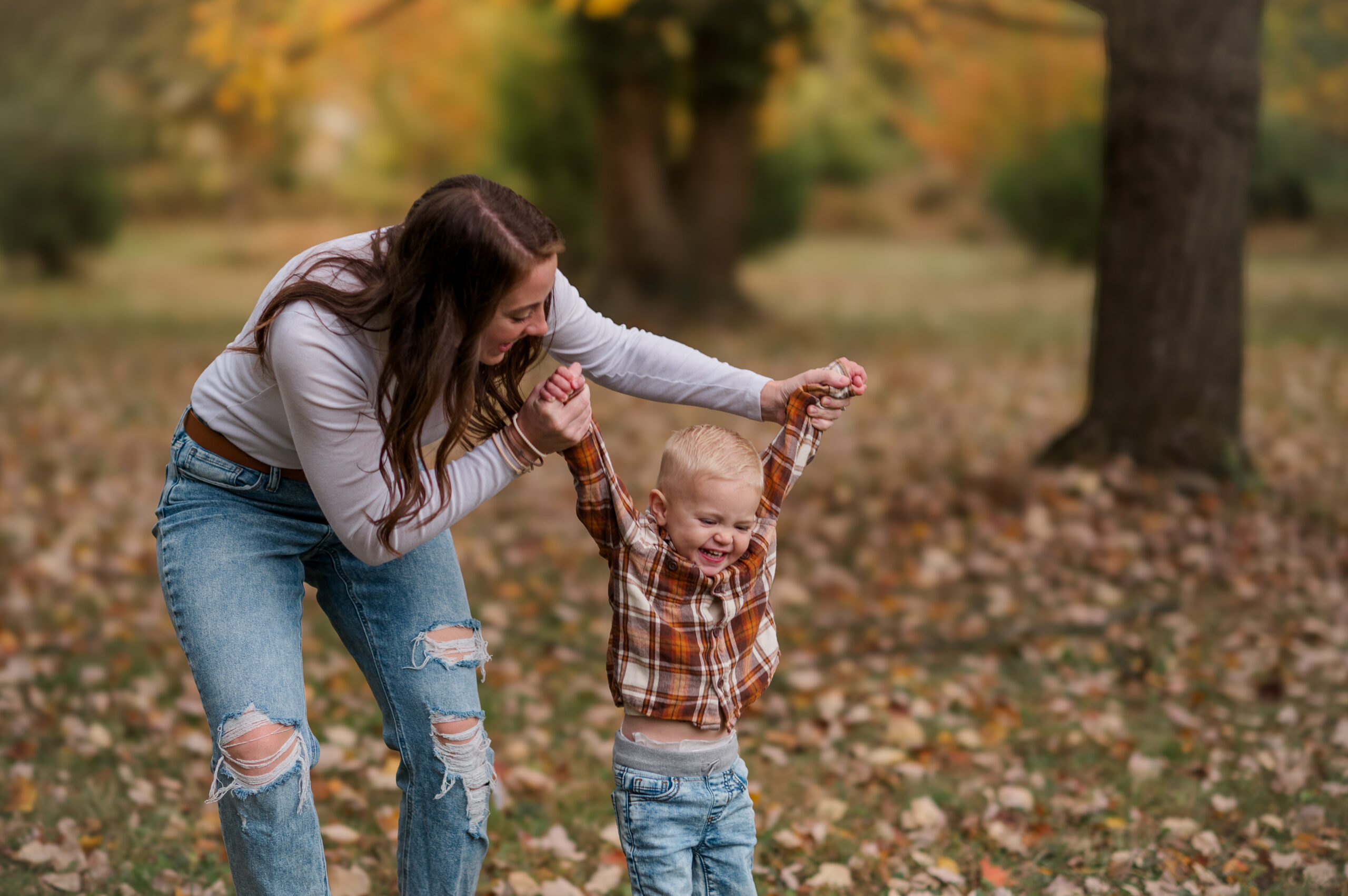 Mom holding her young son’s hands as they play together among the fall leaves during a family photography session in York, PA