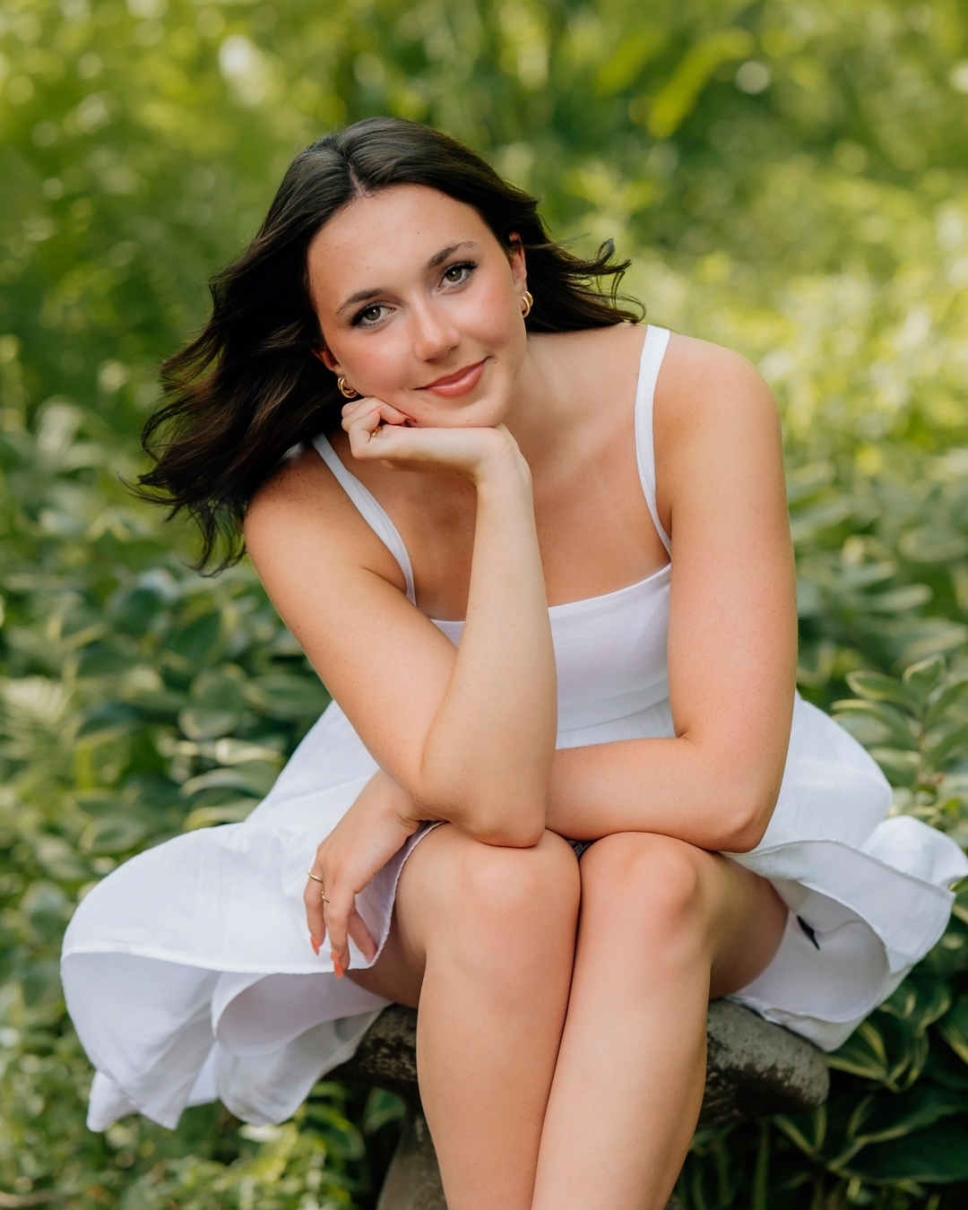 High school senior in a white dress surrounded by a lush garden during senior pictures in Hershey PA