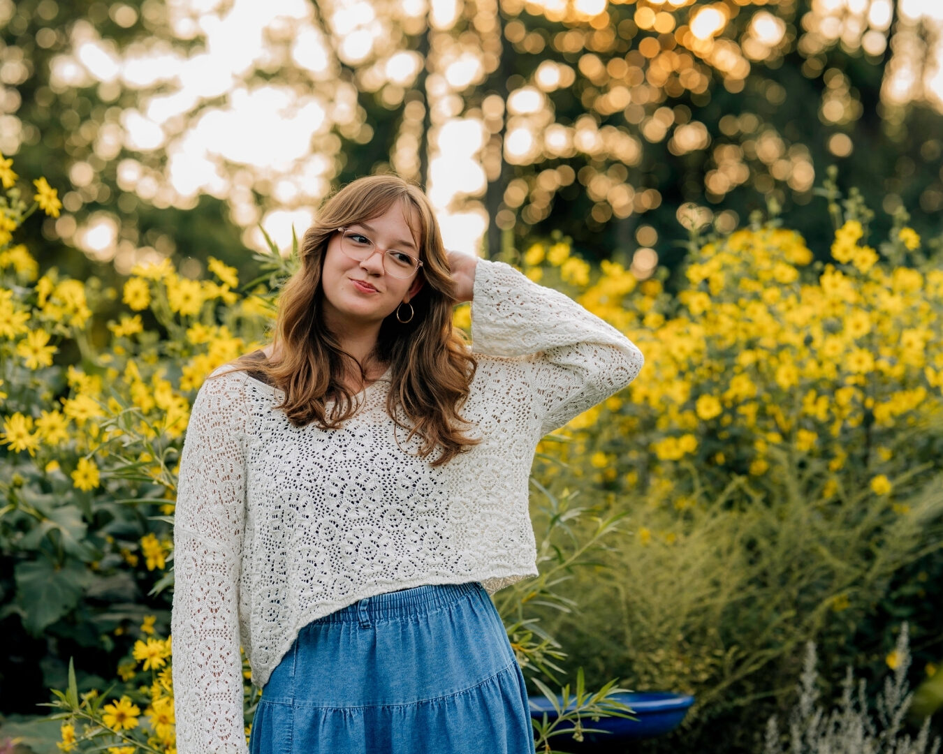 Senior girl wearing a white crochet sweater and blue skirt among yellow flowers in Lancaster PA