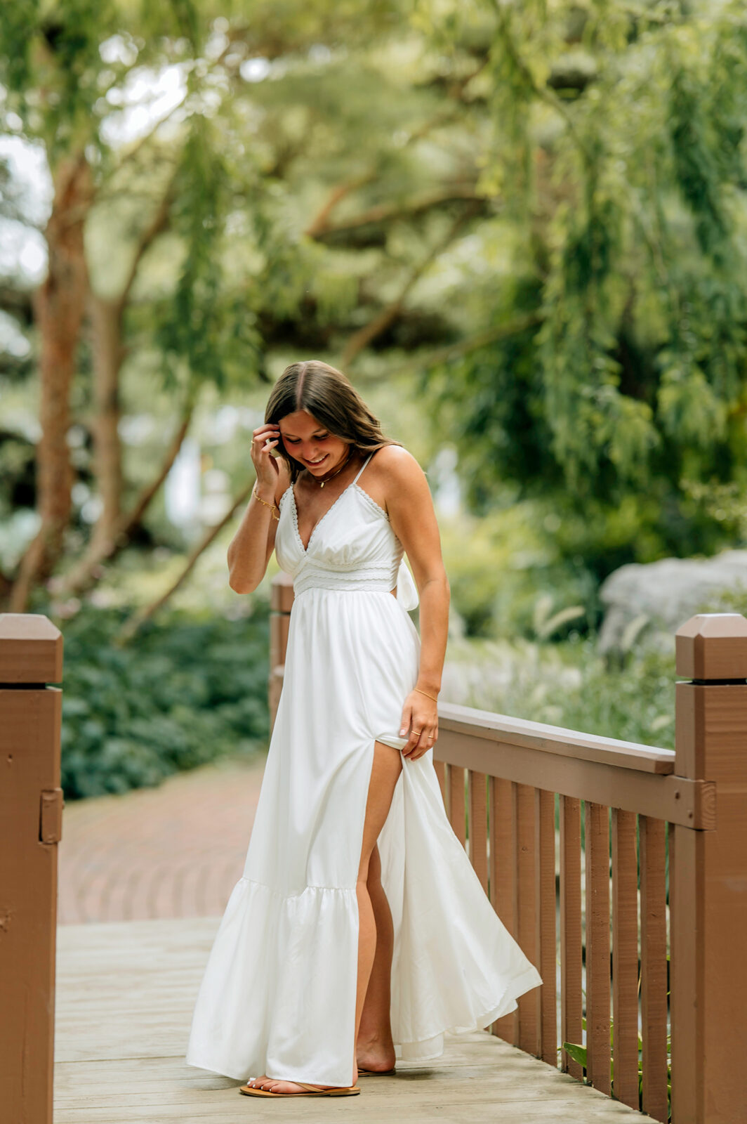 Senior girl in a long white dress walking on a garden bridge during senior pictures in Hershey PA