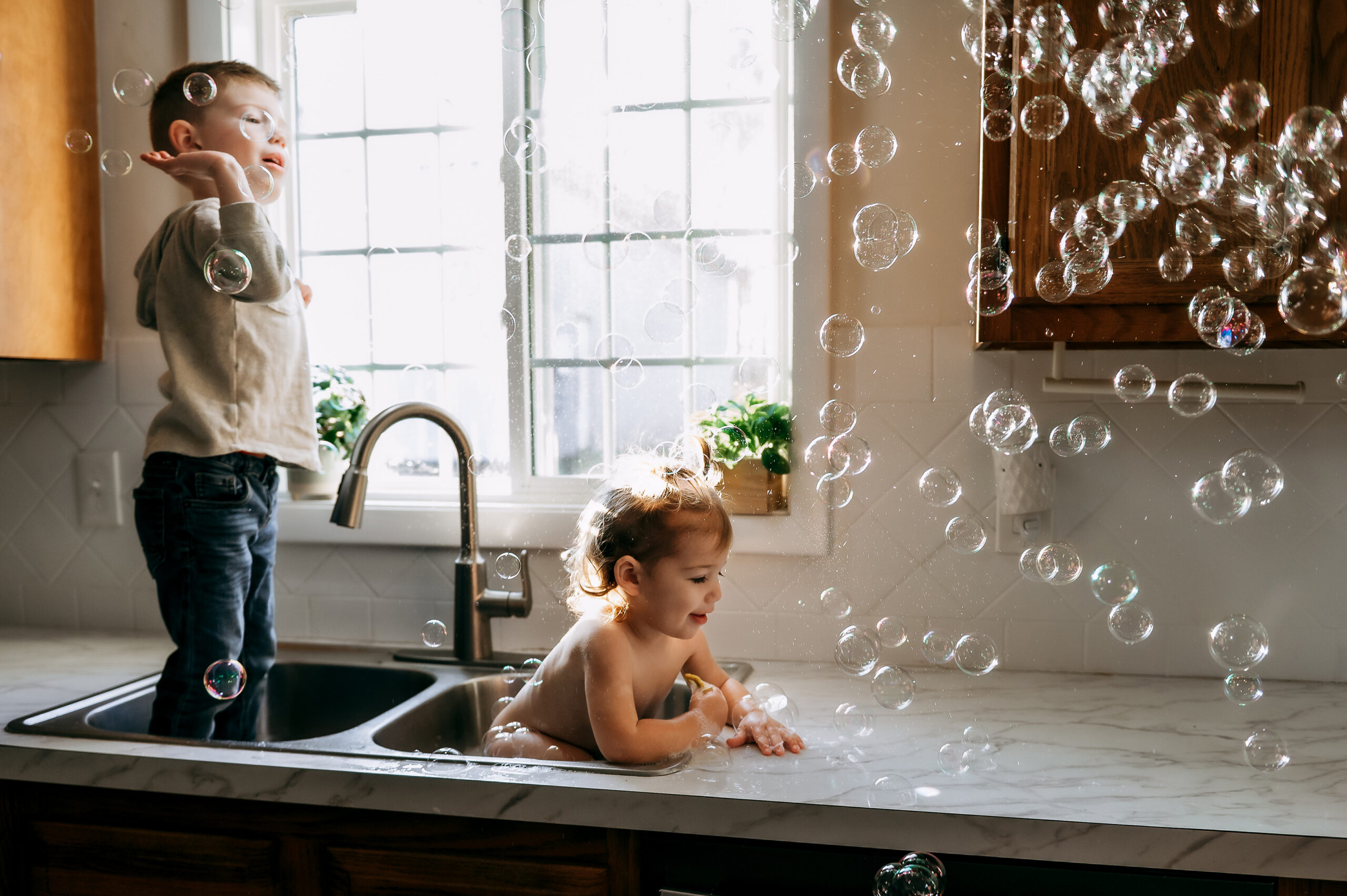 Brother and sister playing together in the kitchen sink during an in-home family photography session